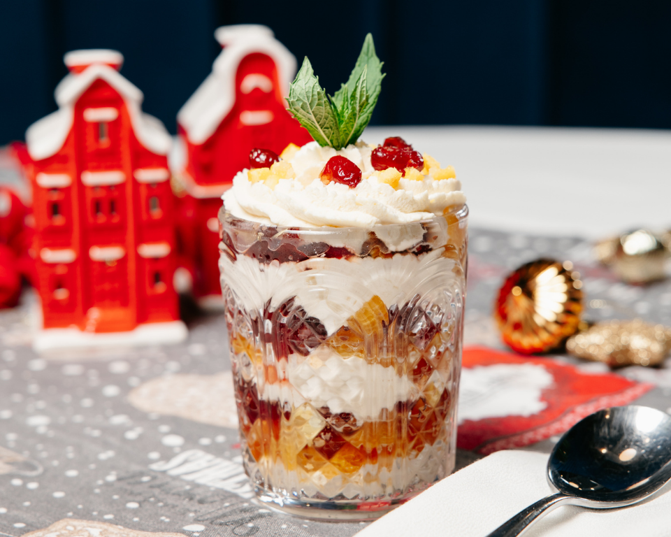 StudioFiveChristmasMenu (1) Festive trifle in a glass with cream, berries and mint on a Christmas table.